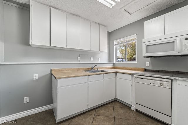 kitchen with white appliances, a sink, dark tile patterned flooring, white cabinets, and a textured ceiling