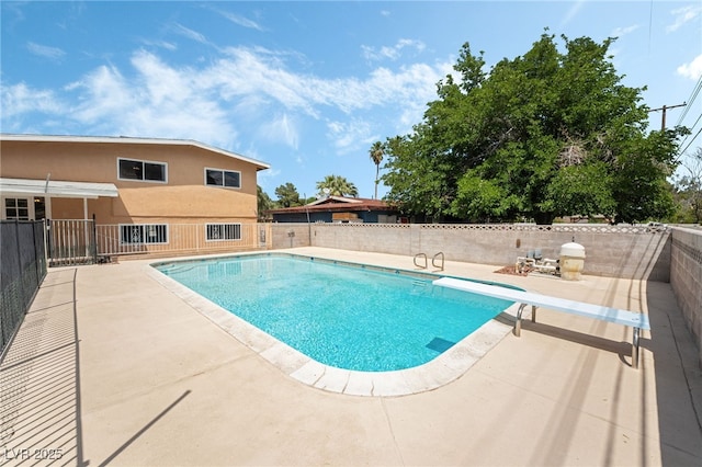 view of pool with a patio, fence, and a diving board