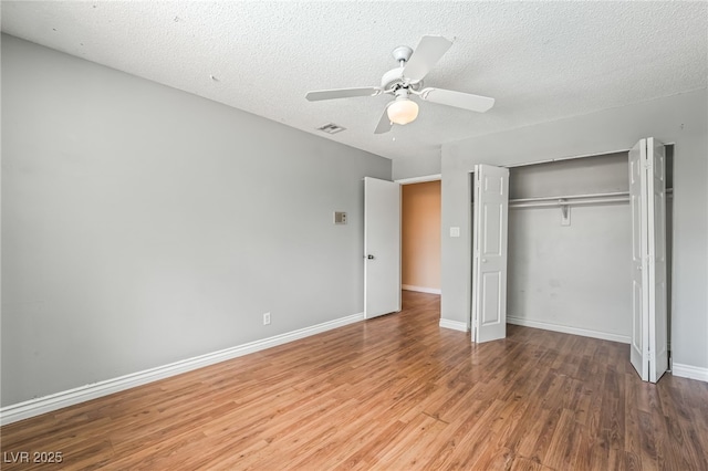 unfurnished bedroom with wood finished floors, a closet, a ceiling fan, baseboards, and a textured ceiling