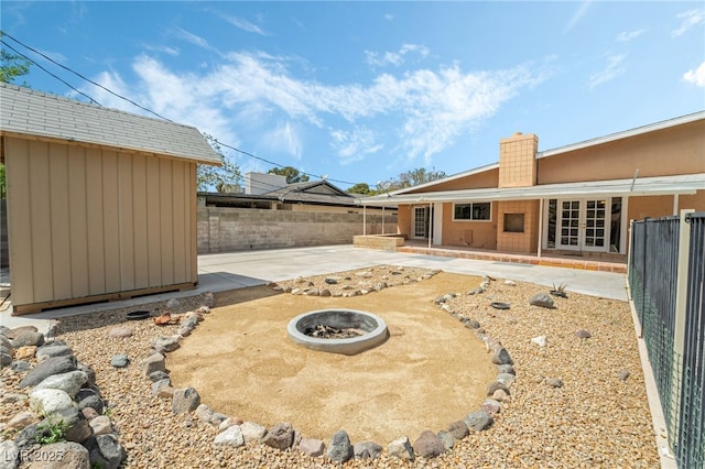 fenced backyard featuring a patio, an outdoor fire pit, an outdoor structure, french doors, and a storage unit