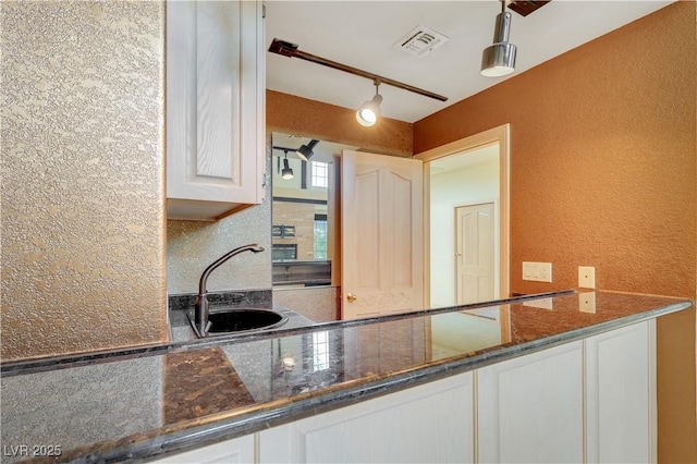 1931 Pago Ct, Las Vegas, NV 89117 - kitchen with a textured wall, dark stone counters, rail lighting, and white cabinetry