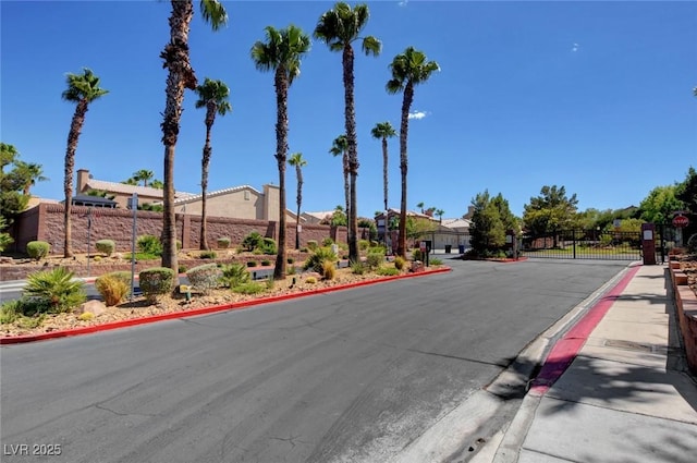 view of asphalt road featuring curbs, a gate, a gated entry, sidewalks, and a residential view