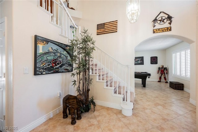stairway with arched walkways, pool table, tile patterned floors, a towering ceiling, and baseboards