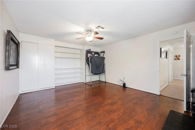 unfurnished room with ceiling fan, wood finished floors, a textured ceiling, baseboards, and built in features