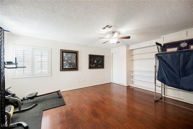 workout area featuring a ceiling fan, dark wood-style floors, and a textured ceiling