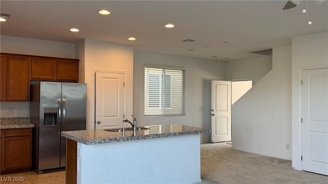 kitchen with stainless steel fridge, a sink, brown cabinetry, stone counters, and recessed lighting