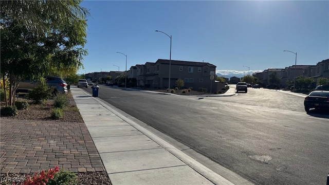 view of asphalt road with a residential view, sidewalks, and street lights