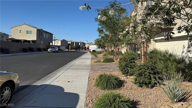 view of asphalt road with sidewalks, street lights, a residential view, and curbs