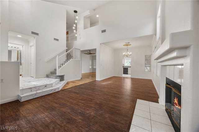 5148 Forest Oaks Dr, Las Vegas, NV 89149 - unfurnished living room featuring a tiled fireplace, wood finished floors, a high ceiling, stairs, and a chandelier
