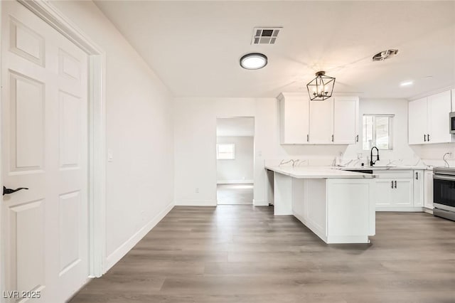kitchen with white cabinetry, a peninsula, light countertops, and wood finished floors