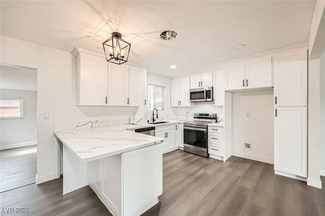 kitchen with appliances with stainless steel finishes, a sink, white cabinets, light stone counters, and dark wood-type flooring