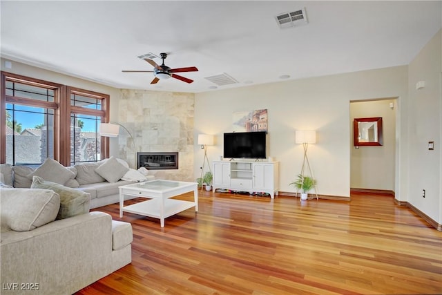 living area featuring ceiling fan, light wood finished floors, baseboards, and a tiled fireplace