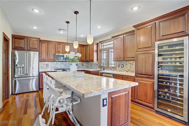 kitchen with stainless steel appliances, beverage cooler, a kitchen island, light wood-style floors, and light stone counters