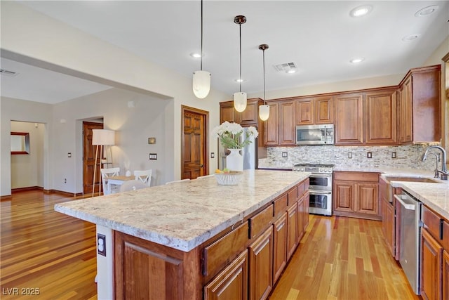 kitchen featuring a sink, stainless steel appliances, brown cabinetry, light wood finished floors, and recessed lighting