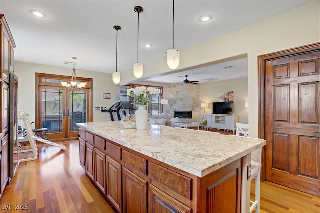 kitchen with ceiling fan, a fireplace, french doors, light wood-style flooring, and a center island