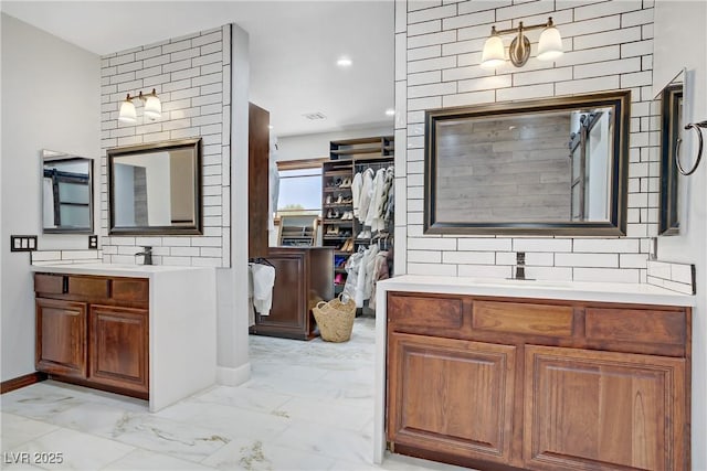 bathroom with marble finish flooring, two vanities, a spacious closet, baseboards, and recessed lighting