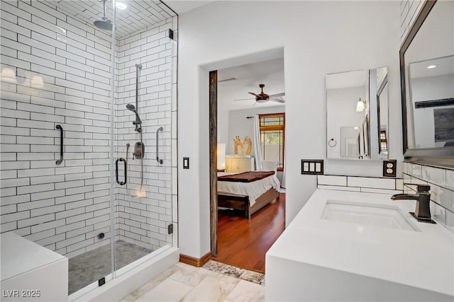 ensuite bathroom with a sink, a shower stall, ceiling fan, marble look tile flooring, and baseboards