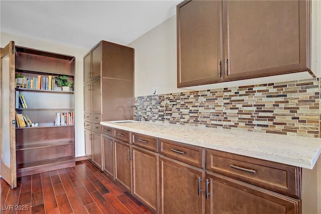 kitchen with a sink, light stone counters, dark wood-style floors, and decorative backsplash