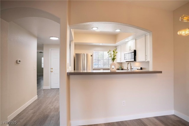 6160 Rumrill St Unit 121, Las Vegas, NV 89113 - kitchen featuring appliances with stainless steel finishes, arched walkways, wood finished floors, white cabinets, and baseboards