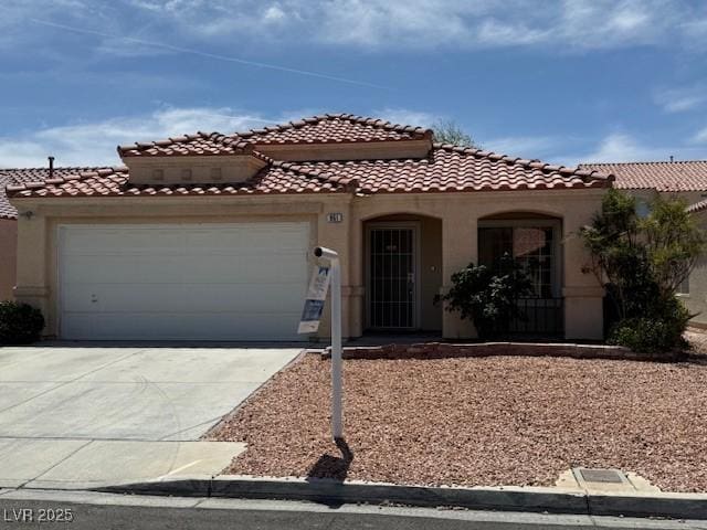 mediterranean / spanish-style home with stucco siding, a tile roof, an attached garage, and driveway