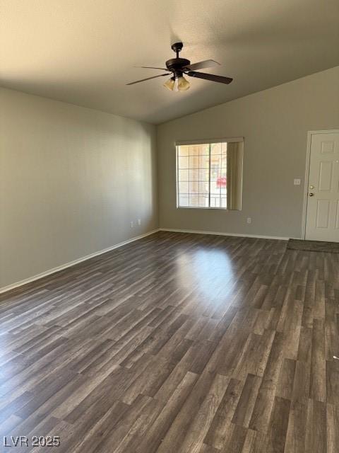 unfurnished room featuring vaulted ceiling, dark wood-style floors, a ceiling fan, and baseboards