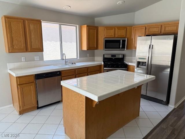 kitchen with stainless steel appliances, tile counters, a sink, and a center island