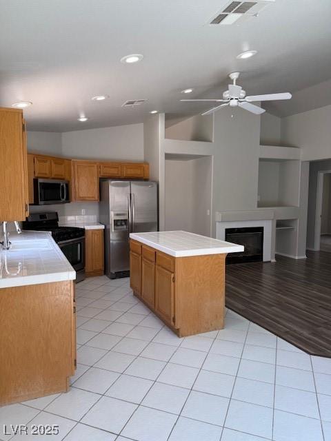 kitchen featuring stainless steel appliances, light countertops, a ceiling fan, a kitchen island, and a fireplace