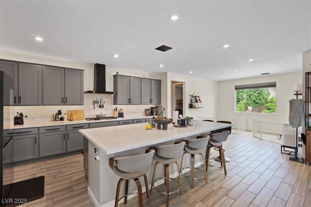 9710 Hiking Ave, Las Vegas, NV 89166 - kitchen featuring wall chimney range hood, stainless steel gas stovetop, wood finish floors, a breakfast bar area, and light countertops
