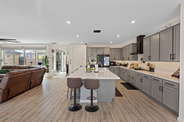 9710 Hiking Ave, Las Vegas, NV 89166 - kitchen with gray cabinetry, wall chimney exhaust hood, open floor plan, appliances with stainless steel finishes, and a kitchen bar