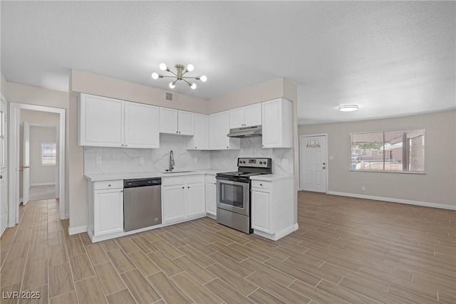 kitchen featuring stainless steel appliances, under cabinet range hood, a sink, baseboards, and light countertops