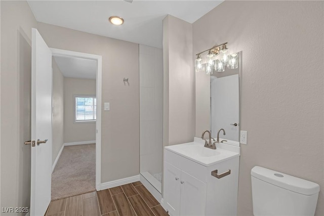 bathroom with toilet, wood finish floors, vanity, a shower, and baseboards