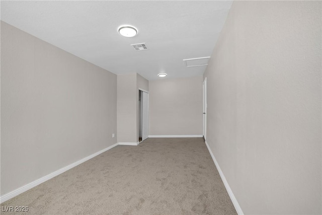 carpeted spare room with attic access and baseboards