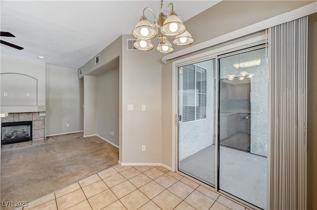 unfurnished dining area featuring a chandelier, ceiling fan, light tile patterned flooring, a tile fireplace, and baseboards