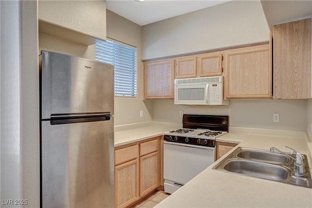 kitchen with white appliances, light brown cabinetry, a sink, and light countertops