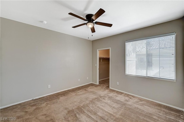 unfurnished bedroom featuring light carpet, baseboards, a walk in closet, ceiling fan, and a closet