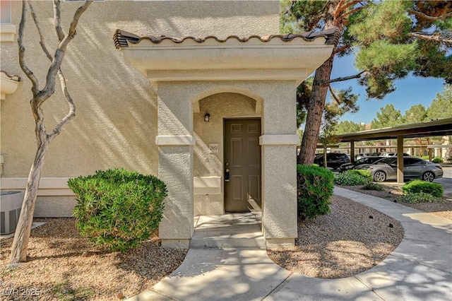 property entrance featuring stucco siding, cooling unit, and covered parking