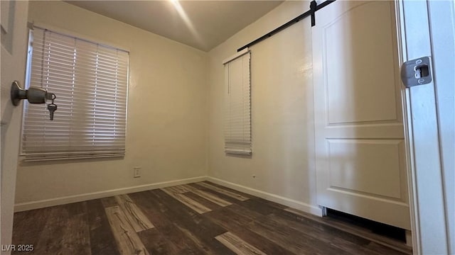 unfurnished bedroom with a barn door, baseboards, and wood finished floors