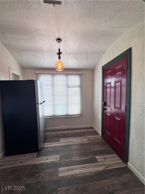 unfurnished dining area with wood finished floors, a textured ceiling, baseboards, and a textured wall