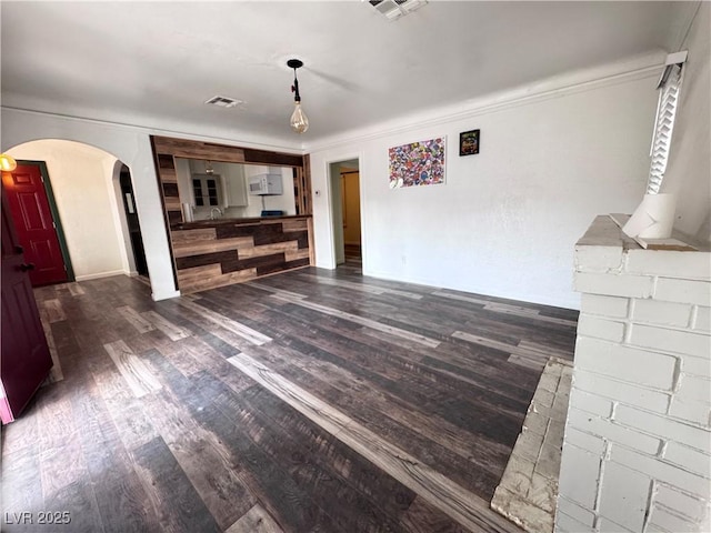 unfurnished living room with arched walkways, wood finished floors, crown molding, and baseboards