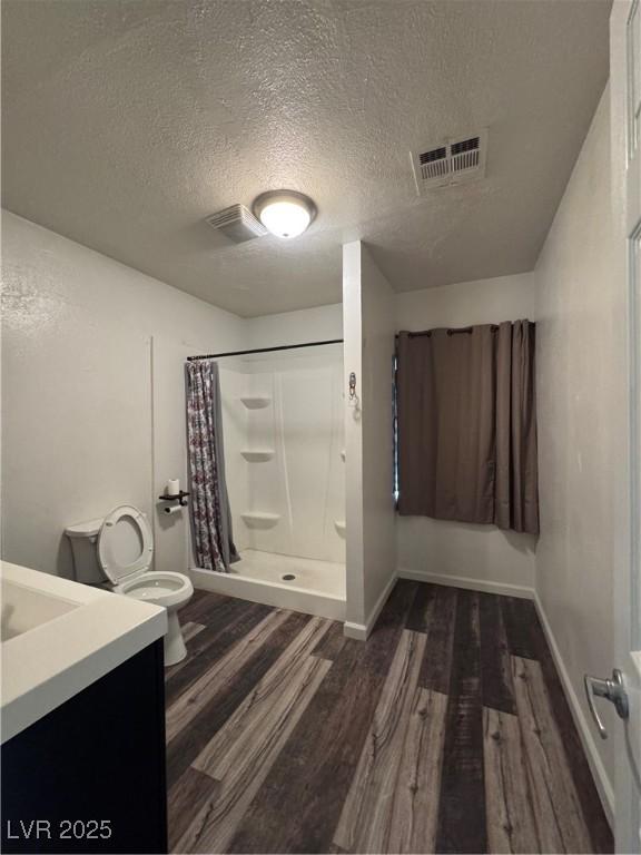 bathroom featuring wood finished floors, a shower stall, toilet, a textured ceiling, and baseboards