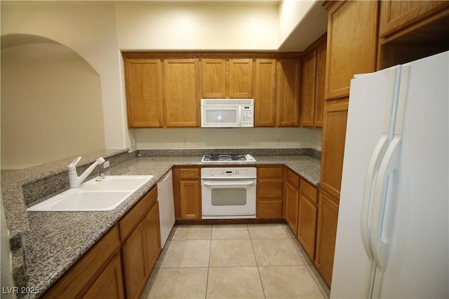 62 E Serene Ave Unit 129, Las Vegas, NV 89123 - kitchen with white appliances, a sink, brown cabinetry, light tile patterned floors, and dark stone countertops