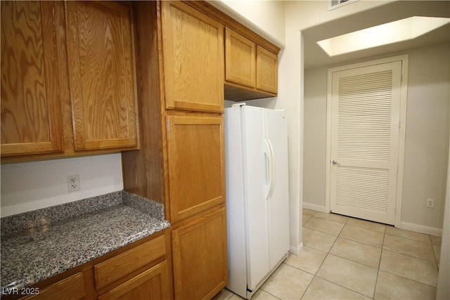 62 E Serene Ave Unit 129, Las Vegas, NV 89123 - kitchen with freestanding refrigerator, light tile patterned floors, dark stone counters, brown cabinets, and baseboards