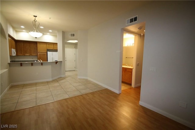 62 E Serene Ave Unit 129, Las Vegas, NV 89123 - kitchen with white appliances, brown cabinetry, light wood-type flooring, a breakfast bar area, and hanging light fixtures