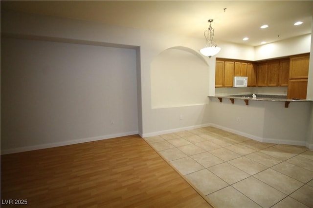 62 E Serene Ave Unit 129, Las Vegas, NV 89123 - kitchen with white microwave, a kitchen bar, light wood-style floors, recessed lighting, and brown cabinets
