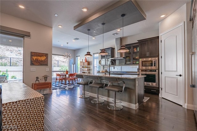 125 Mirage View Dr, Henderson, NV 89011 - kitchen featuring stainless steel appliances, a kitchen breakfast bar, dark brown cabinetry, dark wood-type flooring, and glass insert cabinets