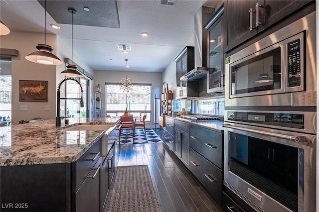 125 Mirage View Dr, Henderson, NV 89011 - kitchen featuring appliances with stainless steel finishes, a chandelier, dark wood-style flooring, glass insert cabinets, and light stone counters