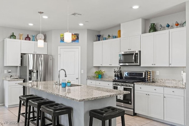 kitchen with stainless steel appliances, a sink, a kitchen bar, light tile patterned flooring, and white cabinetry