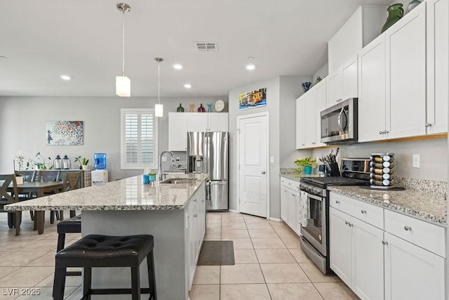 kitchen with stainless steel appliances, a sink, light tile patterned floors, light stone countertops, and white cabinets
