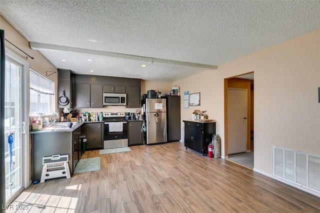 kitchen featuring appliances with stainless steel finishes, a textured ceiling, light wood finished floors, recessed lighting, and a sink