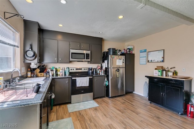 kitchen featuring stainless steel appliances, a sink, light wood finished floors, recessed lighting, and dark countertops